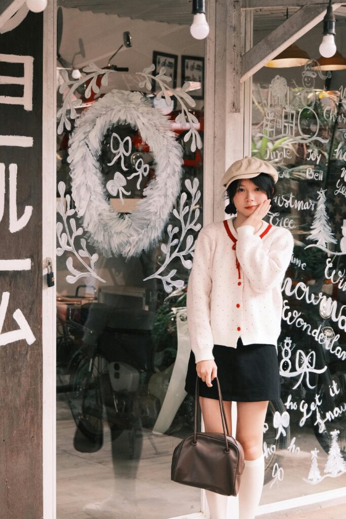 Woman in stylish winter outfit poses outside a festive, decorated cafe with Christmas themes.
