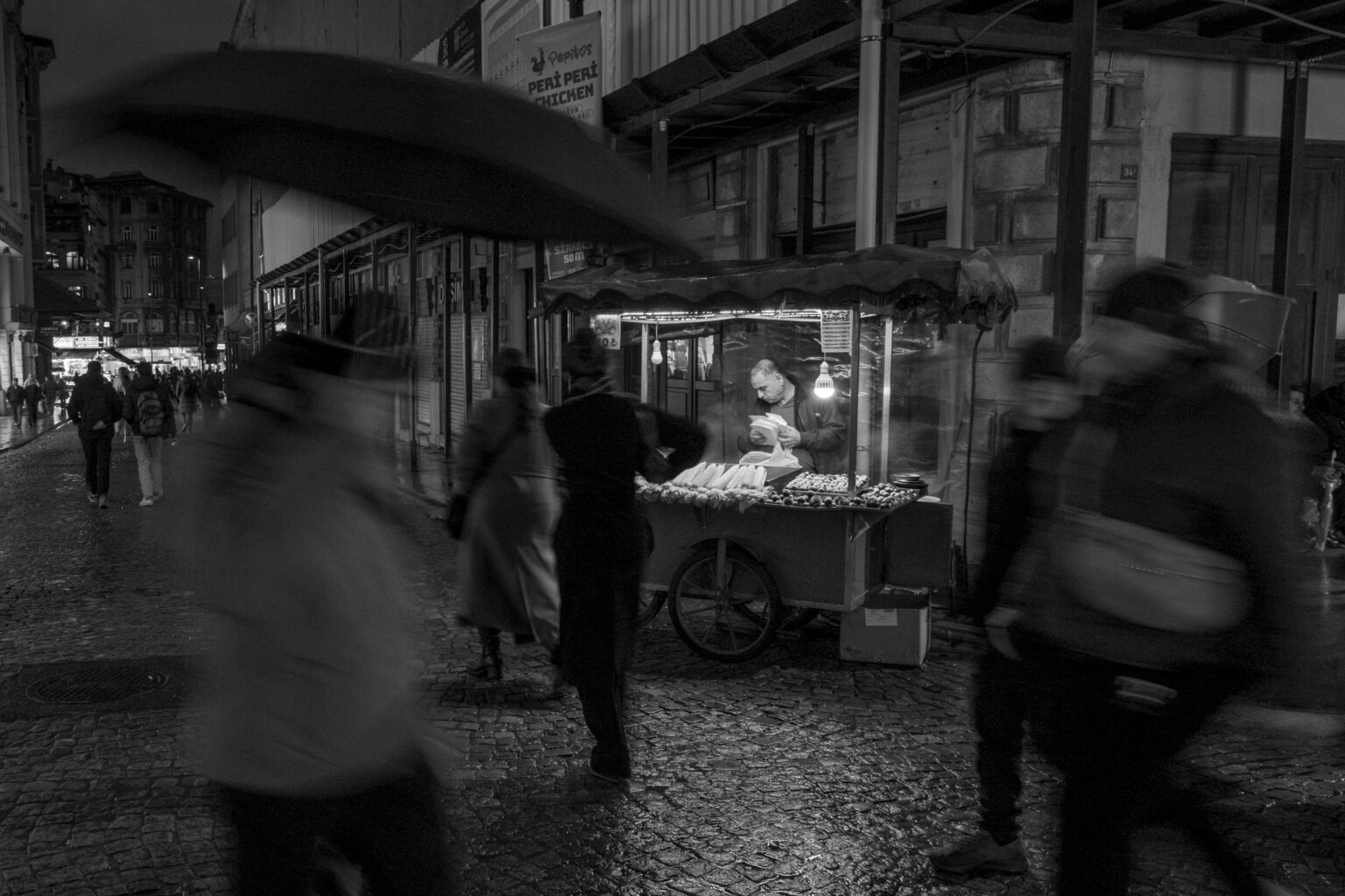A bustling city street with a night vendor selling food, captured in black and white.