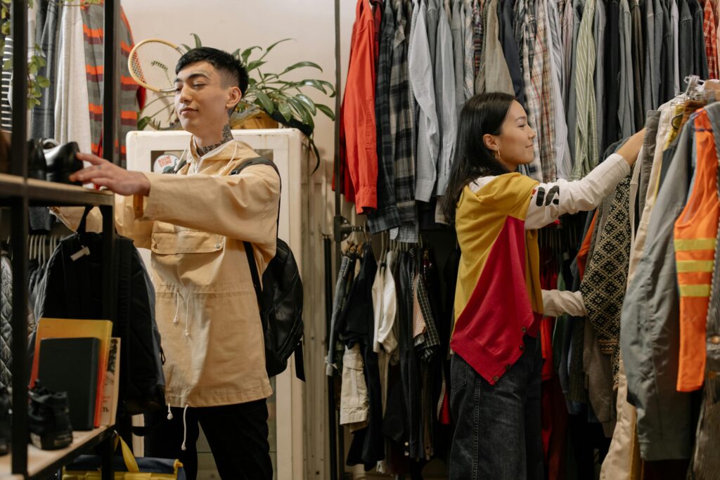Two young adults selecting clothes in a crowded vintage thrift store.