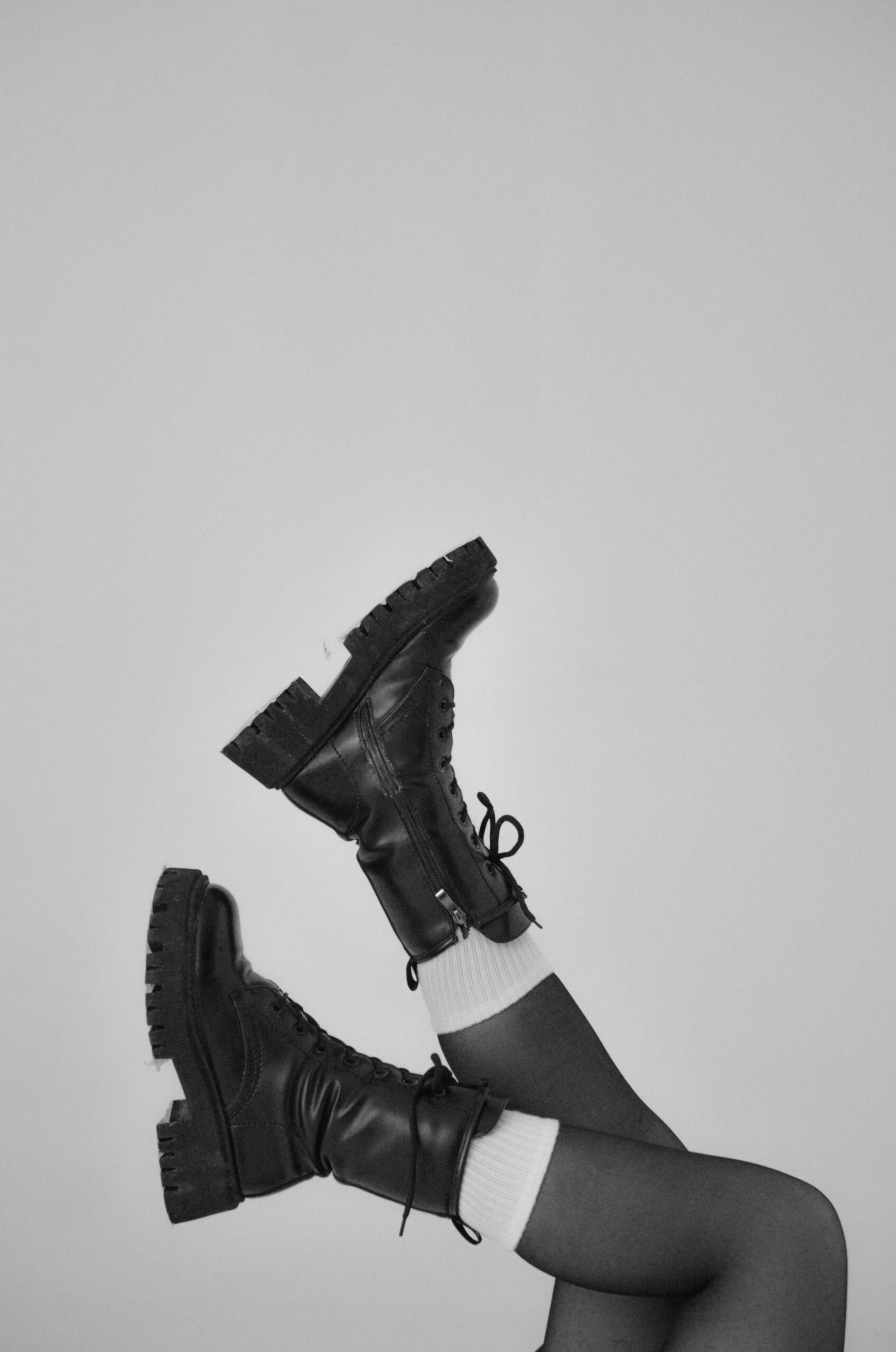 Black leather boots paired with white socks in a minimalist vertical composition.