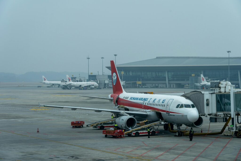 Sichuan Airlines Airbus A320 parked at a busy airport terminal under a cloudy sky.